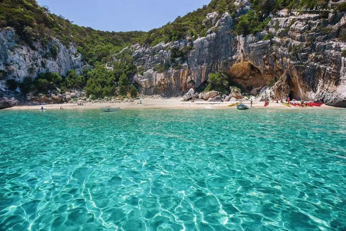 Una spiaggia con acqua cristallina vicino ad una scogliera rocciosa. Situata a Cala Gonone, questa pittoresca spiaggia offre un rifugio tranquillo al Club Esse Beach Village.