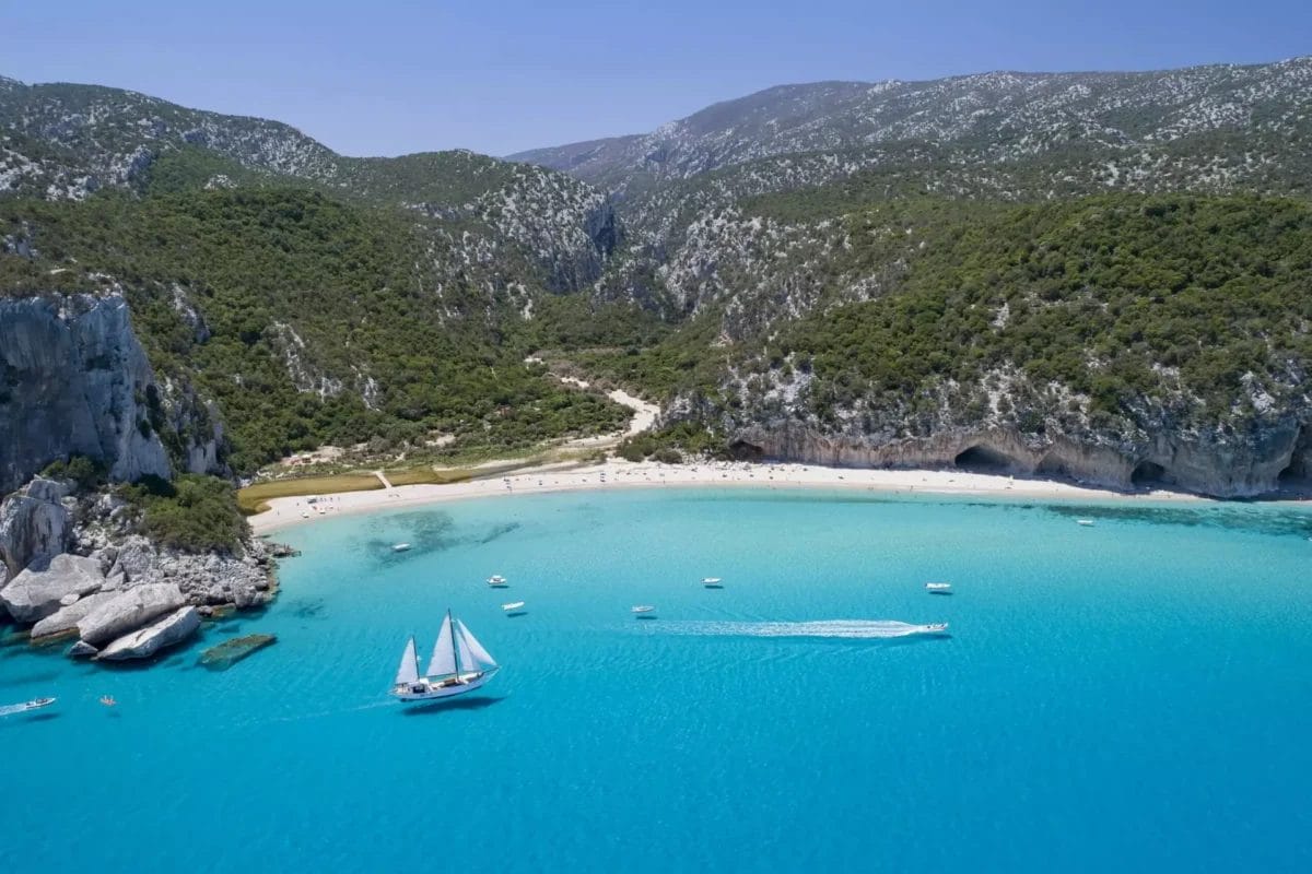 Veduta aerea di una spiaggia con barca a vela in acqua, situata nel Club Esse Cala Gonone.