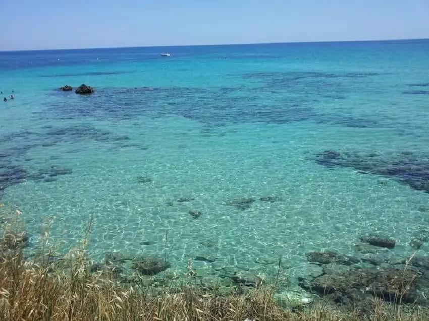 Un oceano cristallino con una zona erbosa vicino, situato presso il Nicolaus Club Fontane Bianche.