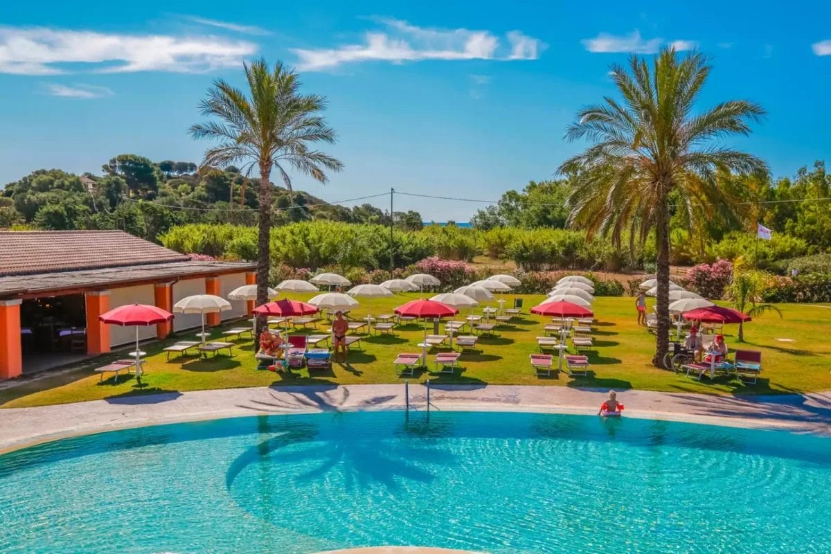 ALMA RESORT dispone di una piscina con ombrelloni e sedie, circondata da palme.