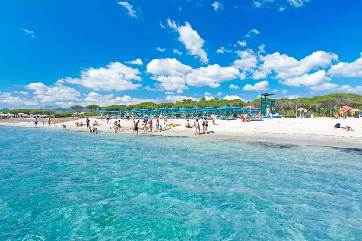 Una vivace spiaggia a Budoni con una moltitudine di persone che si godono il sole e l'acqua.