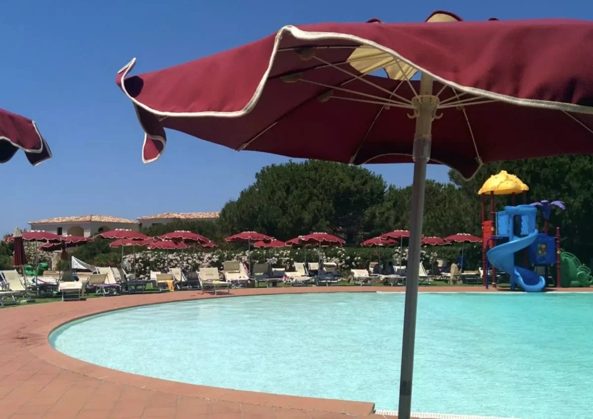 Una piscina con ombrellone rosso presso uno stabilimento balneare di Esse Gallura.