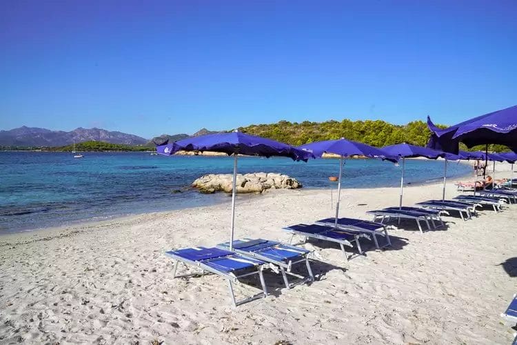 Una spiaggia con sedie FUTURA CLUB e ombrelloni BAJA BIANCA sulla sabbia.