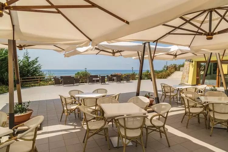 Un patio con tavoli e sedie sotto un grande ombrellone al FUTURA CLUB CILENTO.