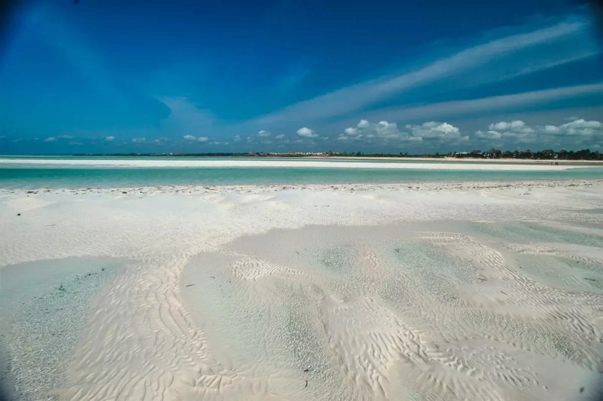 Una spiaggia di sabbia bianca con un cielo azzurro e sabbia bianca, ideale per una rilassante esperienza in un resort sulla spiaggia.