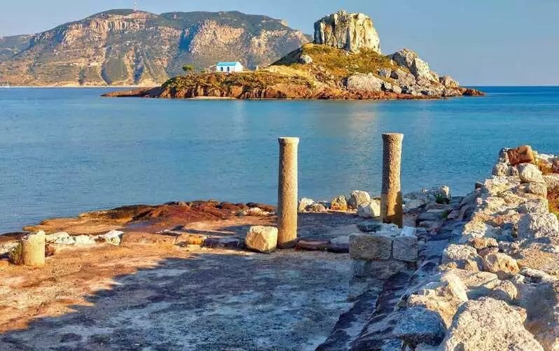 Una piccola isola con pilastri e una roccia nell'acqua, situata vicino a VERACLUB KOS.