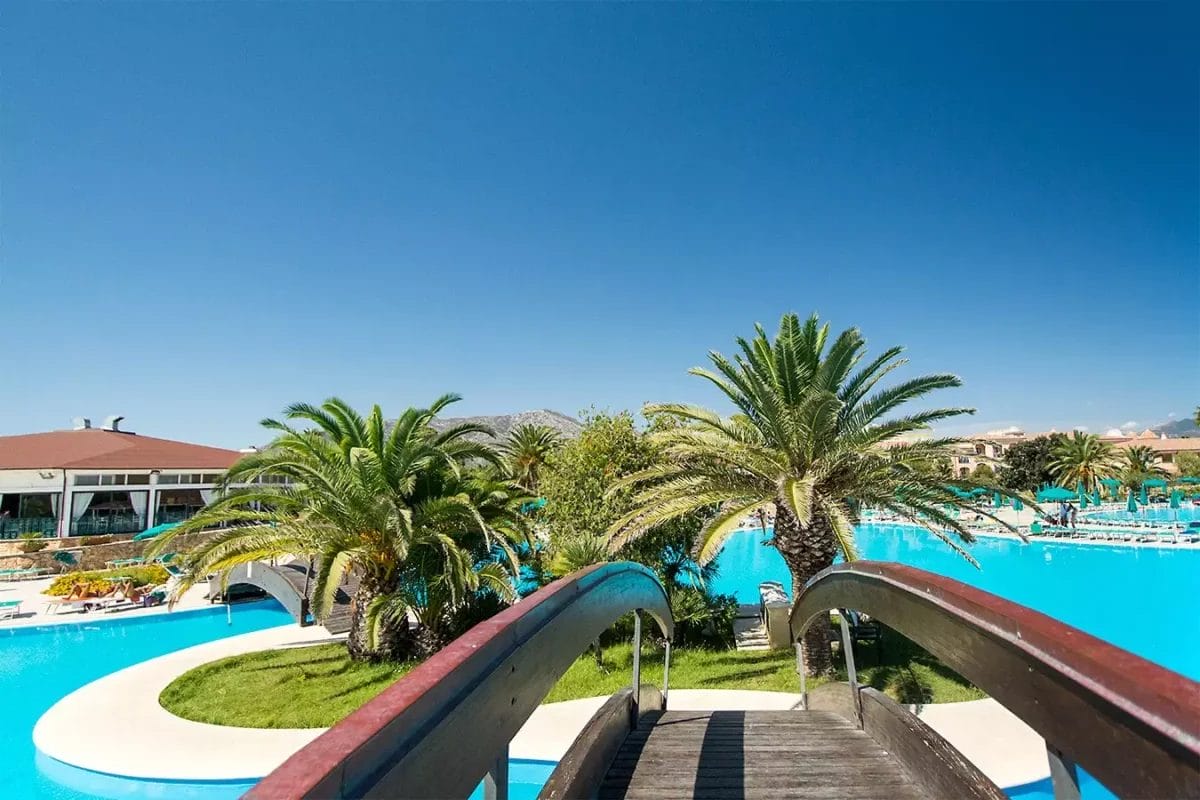 Una passerella che conduce ad una piscina circondata da palme presso un beach club.