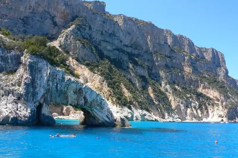 Un gruppo di persone sta nuotando nell'acqua blu vicino ad uno stabilimento balneare.