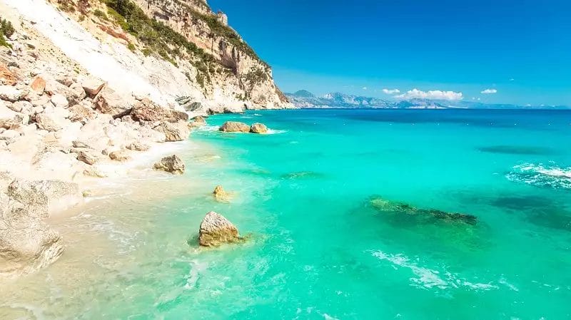 Una veduta aerea di una spiaggia con acqua blu e scogliere, vista da un resort sul porto.