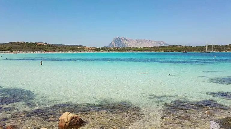 Una spiaggia con acqua limpida e una montagna sullo sfondo, situata nei pressi del FUTURA CLUB.