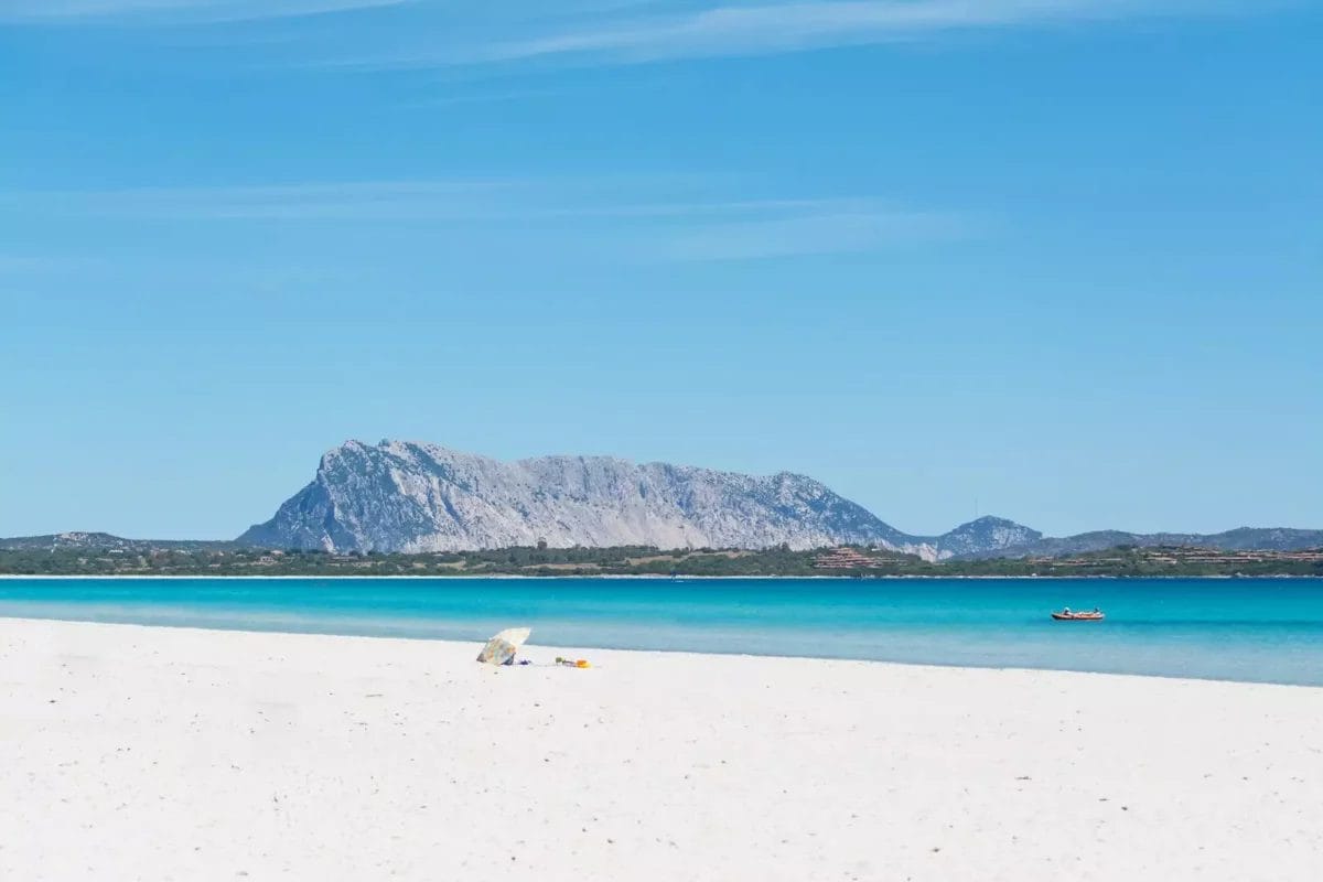 Una spiaggia di sabbia bianca con una montagna sullo sfondo, circondata dalla bellezza di BAJA BIANCA.