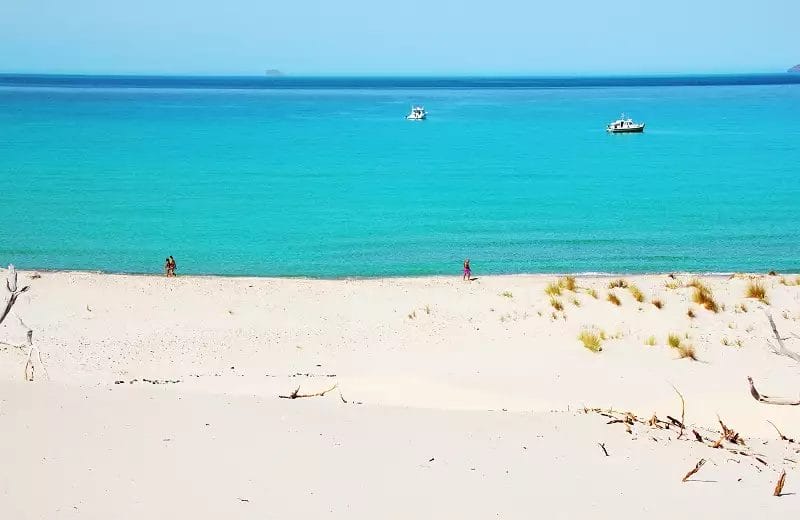 Una spiaggia con dune di sabbia e barche in acqua a Porto Pino.