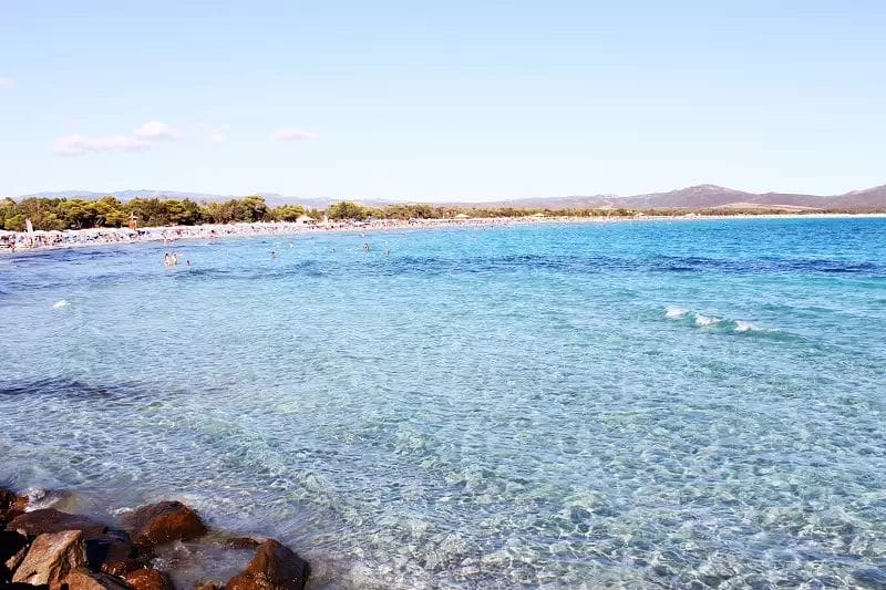 Una spiaggia con acqua limpida e gente che ci nuota.