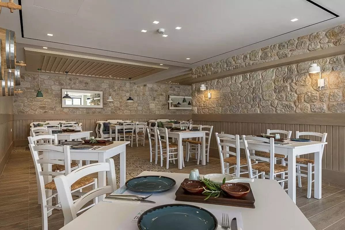 Un ristorante KOS con tavoli e sedie bianchi e un muro in pietra.