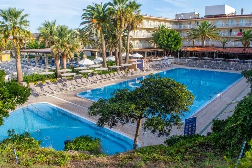 Piscina del resort dell'hotel circondata da lettini e palme con un cielo azzurro limpido aguamarina.