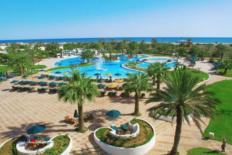 Piscina del resort tropicale con lettini e palme affacciata sull'oceano presso la Thalasso Spa Alpiclub Djerba Plaza.