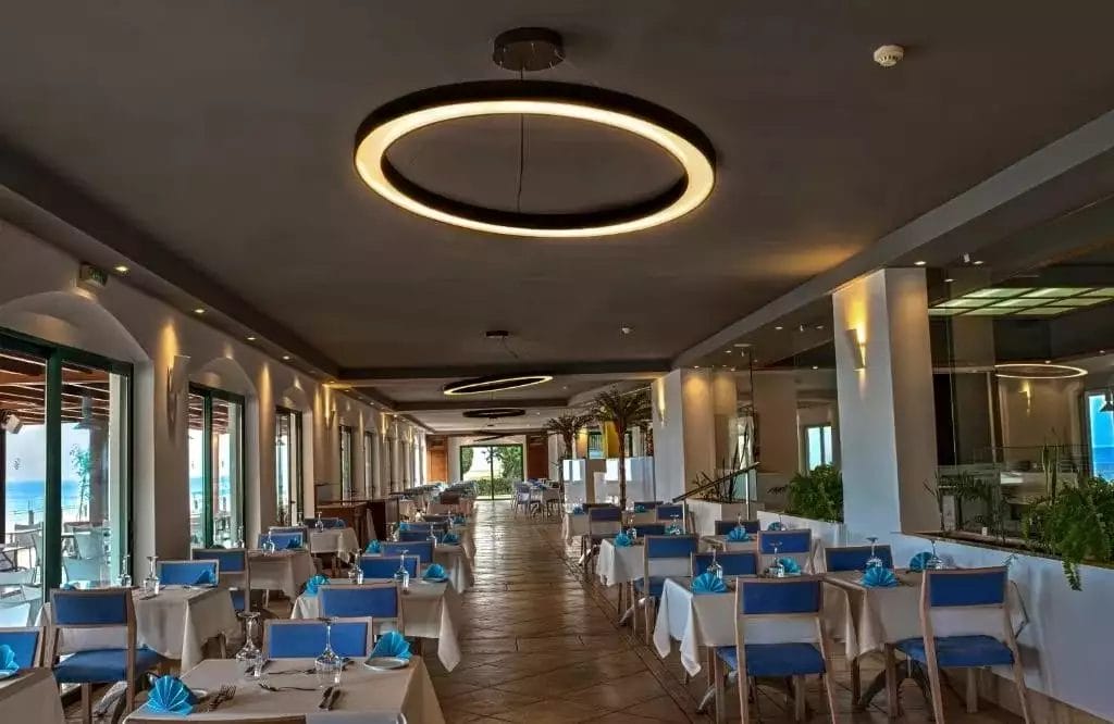 Interni moderni del ristorante con plafoniere circolari, tavoli apparecchiati e grandi finestre presso il lussuoso Apostolata Island Resort & Spa.