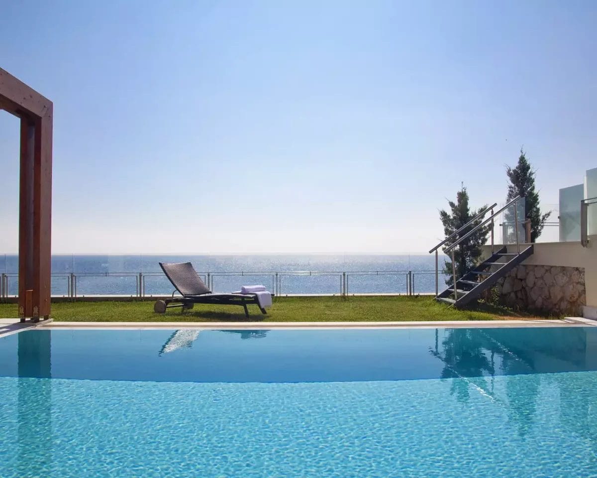 Una piscina a sfioro presso l'Apostolata Island Resort & Spa con vista sul mare con una poltrona lounge singola di fronte all'acqua e scale sulla destra che conducono a un livello superiore.