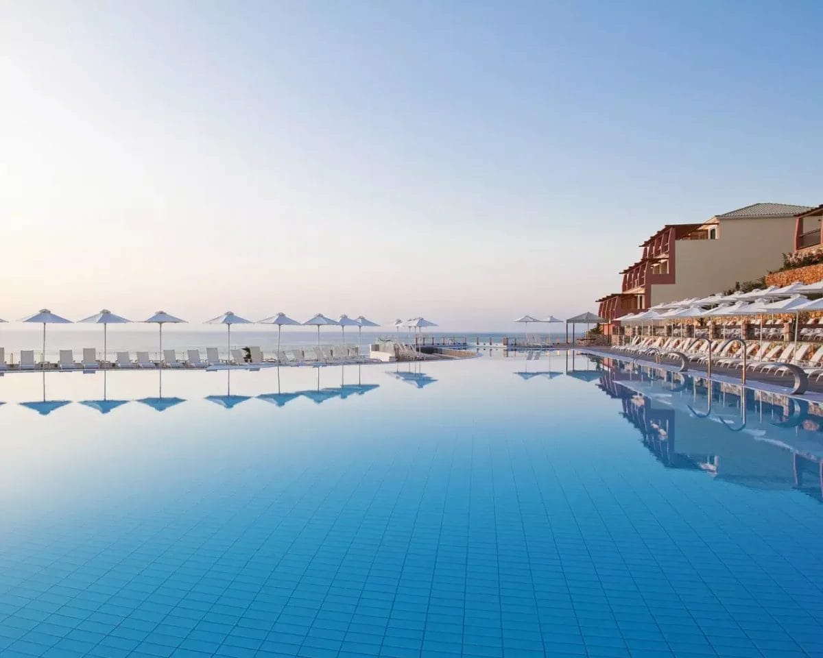 Piscina a sfioro con vista sull'oceano e circondata da sedie a sdraio e ombrelloni all'alba o al tramonto presso Apostolata Island Resort & Spa.