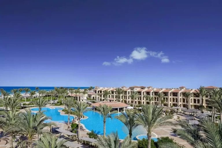 Lussuoso Almaza Beach Resort con piscine e palme affacciate sul mare.