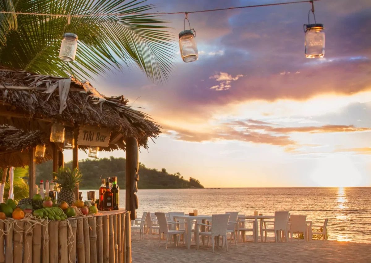 Tiki bar sulla spiaggia al tramonto con lanterne sospese e vista sulla SPIAGGIA BRAVO ANDILANA.