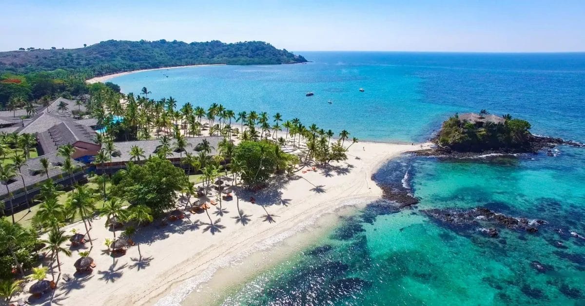 Veduta aerea del Bravo Andilana Beach Resort con palme su una spiaggia sabbiosa, acque cristalline e barche vicino alla costa.