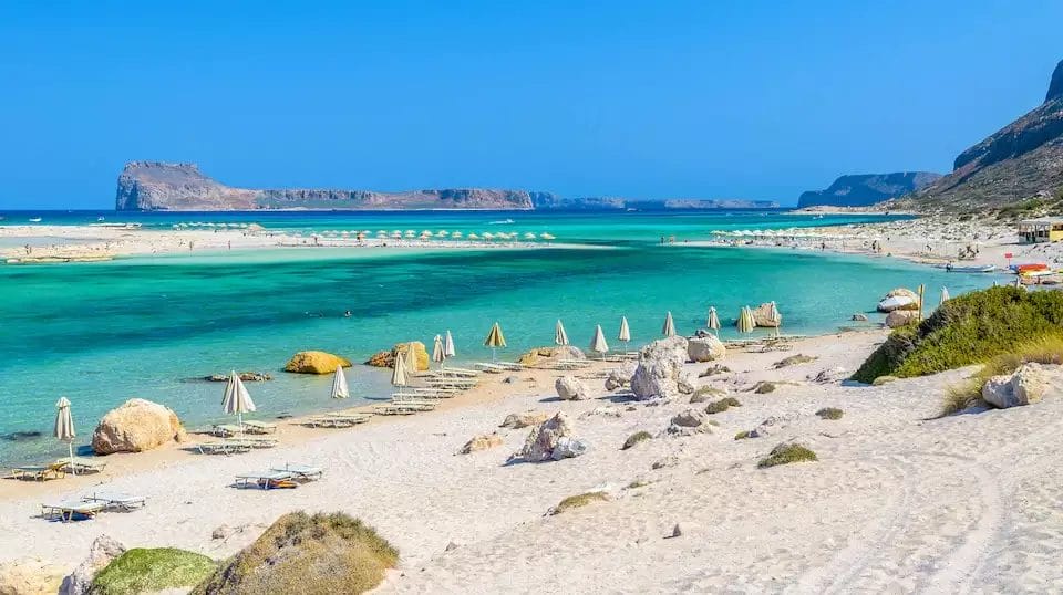 Una serena scena sulla spiaggia del VERACLUB con acque turchesi, sabbia bianca e ombrelloni allineati lungo la riva del CREAN VILLAGGIO.