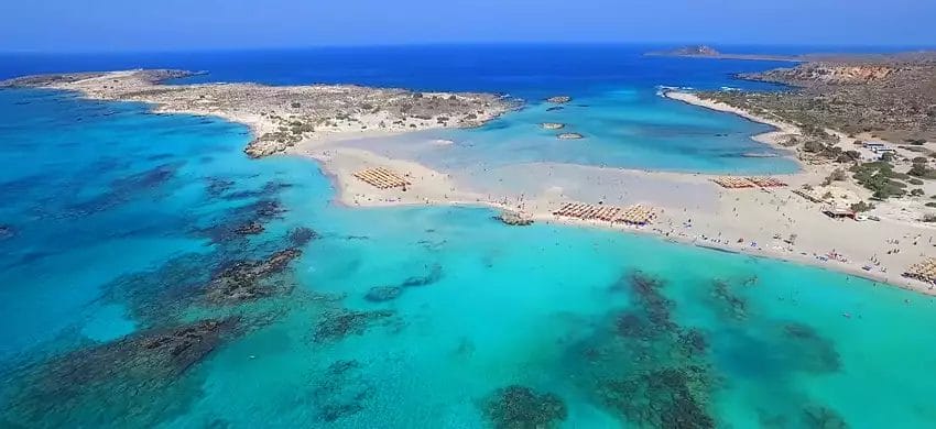 Veduta aerea di una spiaggia tropicale con acque turchesi limpide e bagnanti sulla sabbia vicino al VERACLUB CRETAN Village.