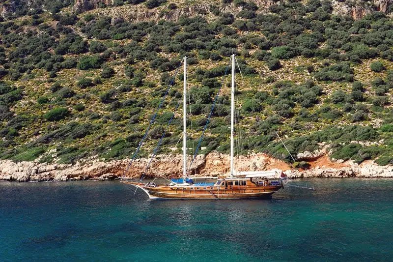 Un tradizionale caicco in legno ancorato in una baia serena con lussureggianti colline verdi sullo sfondo, in Turchia.