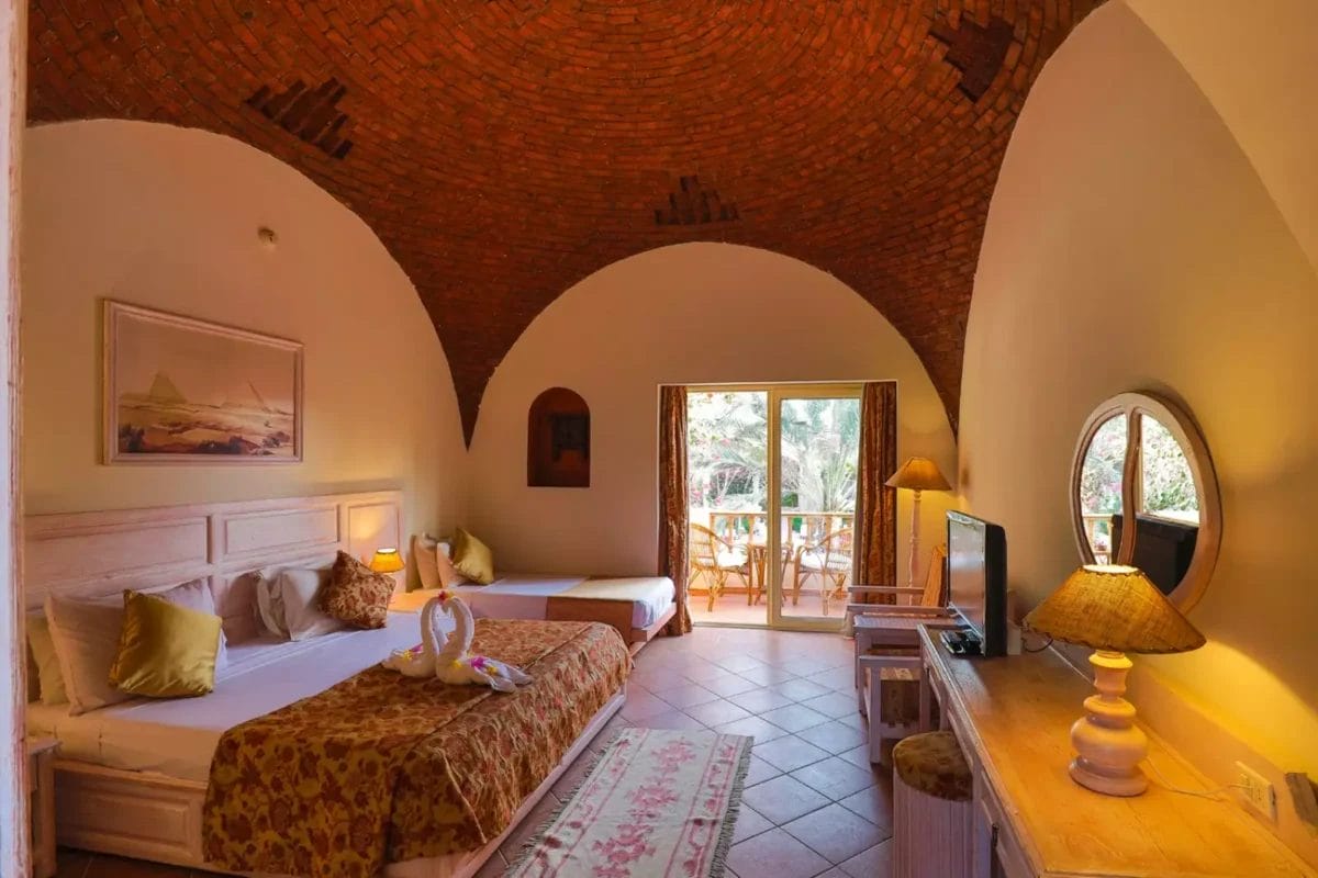 Interno con soffitto a volta di una camera da letto dai toni caldi al Dream Lagoon Resort con porte ad arco, due letti e accesso a un balcone.