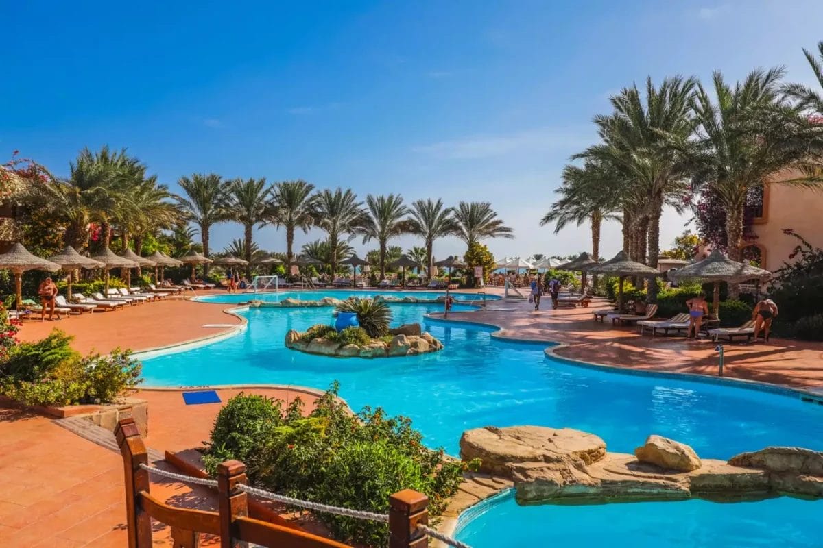 Una vivace area piscina da sogno in un resort lagunare con palme, lettini prendisole e ospiti che si godono il clima soleggiato.