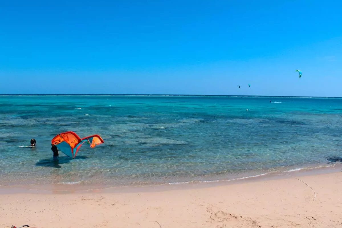 Una persona monta un kiteboard su una spiaggia limpida e poco profonda al Dream Lagoon Resort con altri kiteboarder in lontananza.