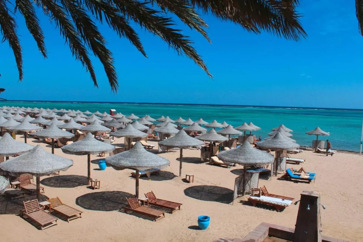 Una tranquilla spiaggia al Dream Lagoon Resort con file di ombrelloni in paglia e lettini che si affacciano su una laguna blu e cristallina.