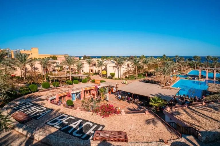 Un pittoresco resort a Sharm El-Sheikh con rigogliose palme, fiori vivaci e invitanti piscine sotto un cielo azzurro e limpido, che offre una vacanza serena sulla spiaggia.