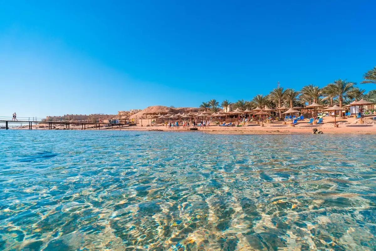 Acque cristalline si avvicinano dolcemente a una spiaggia sabbiosa fiancheggiata da palme, mentre i vacanzieri si godono una giornata di sole nel tranquillo resort BRAVO TAMRA BEACH.