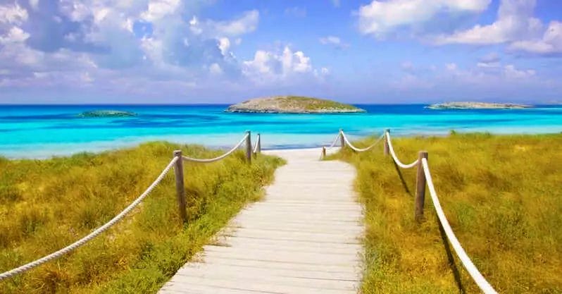 Una passerella in legno che conduce alla spiaggia Seaclub Insotel con acqua blu.