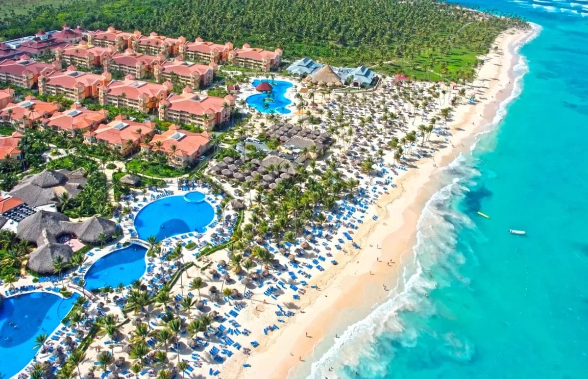 Veduta aerea del resort Grand Bahia Principe Turquesa con piscine e palme lungo un litorale sabbioso.