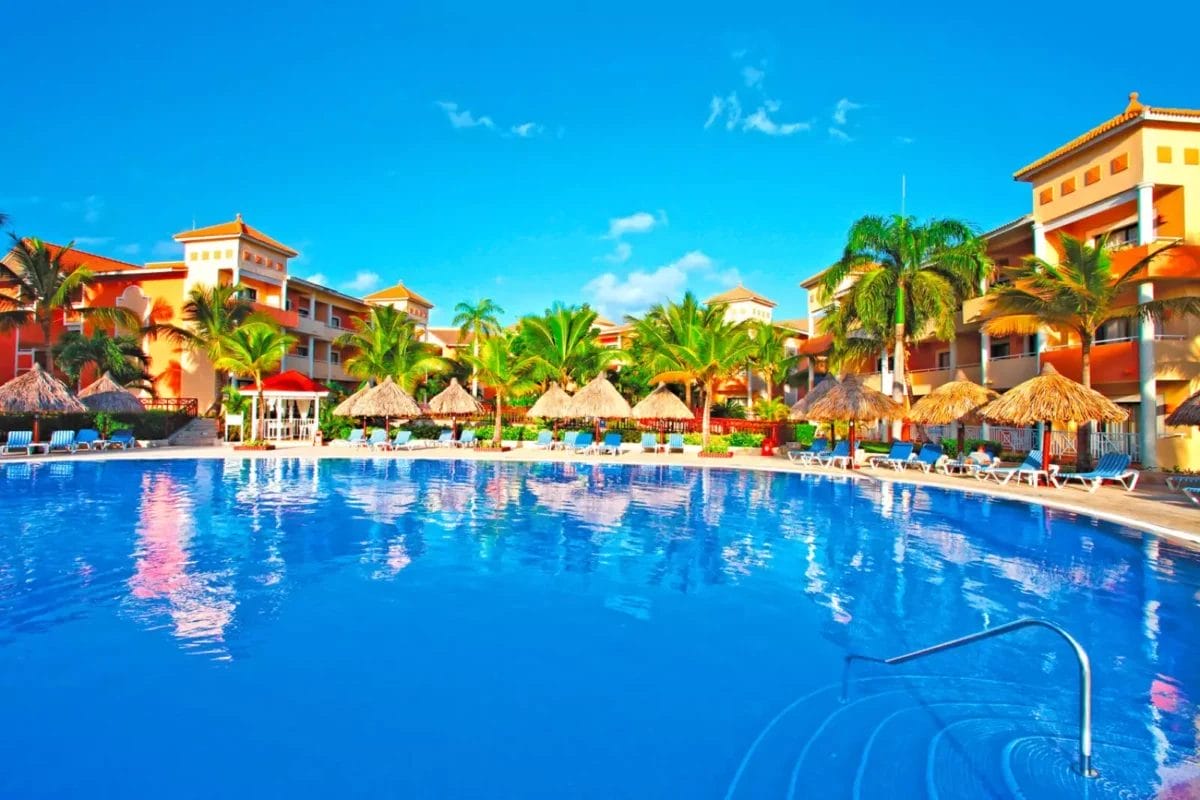 Lussuoso resort Grand Bahia Principe Turquesa con una grande piscina, ombrelloni e palme tropicali sotto un cielo azzurro brillante.