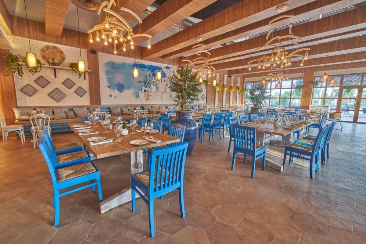 Interni spaziosi e lussuosi del ristorante del resort con sedie blu, tavoli in legno e decorazioni rustiche al Grand Bahia Principe Turquesa.