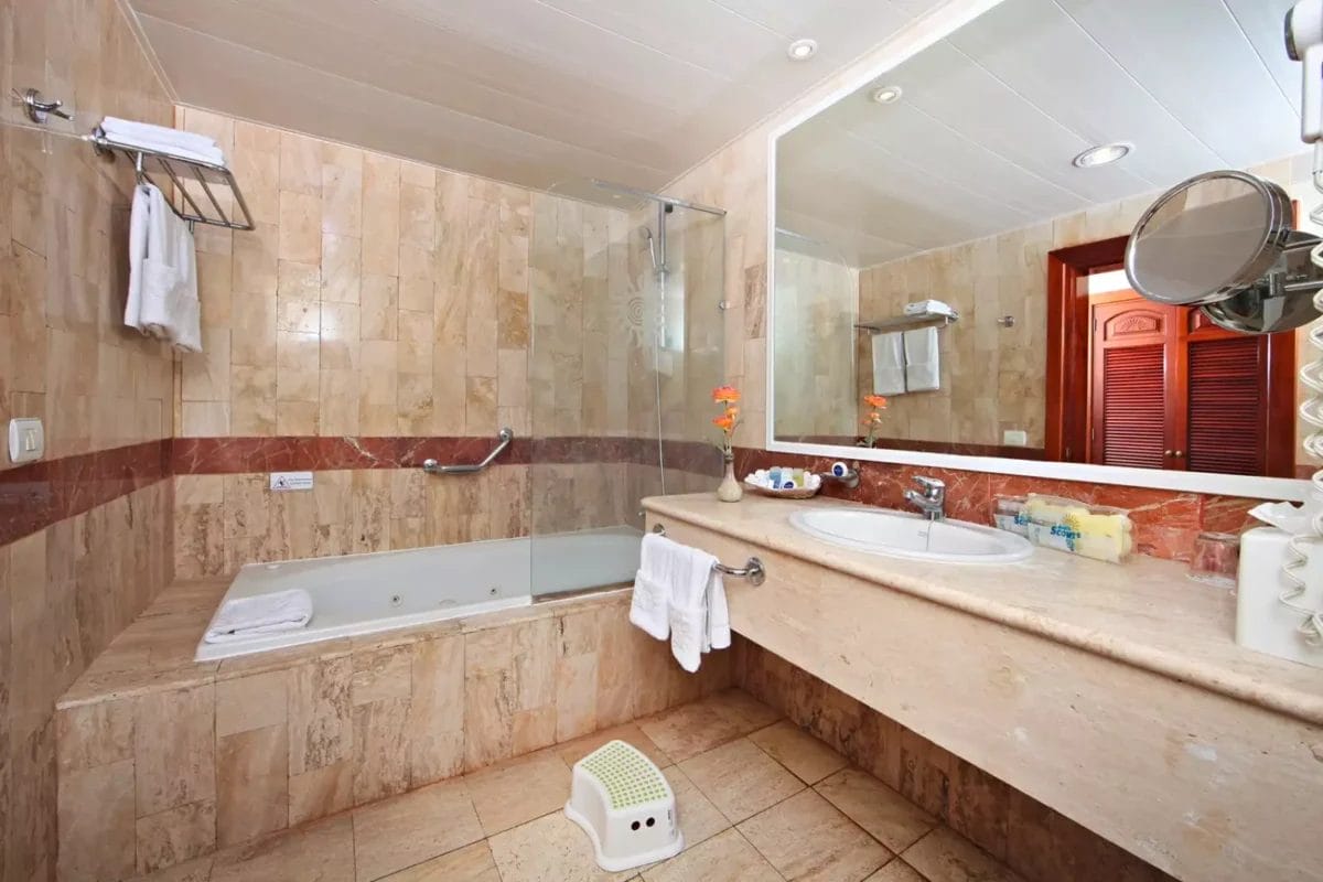 Un bagno moderno con vasca, parete divisoria in vetro, doppio lavabo e piastrelle in marmo nel resort Grand Bahia Principe Turquesa.