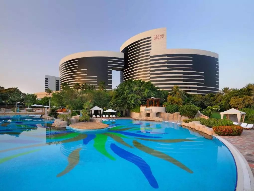 Edifici di hotel di lusso affacciati su una tranquilla piscina con disegni artistici sottomarini, immersi in un giardino paesaggistico presso il Grand Hyatt Dubai.