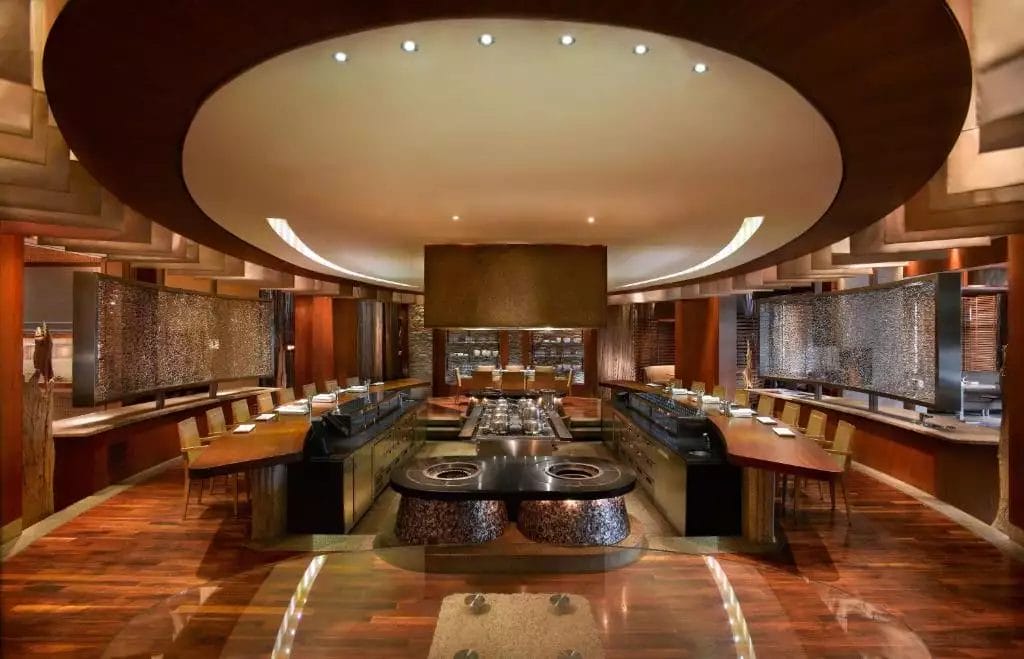 Interni moderni del ristorante all'interno del Grand Hyatt Dubai, caratterizzato da una zona cottura centrale circolare e tavoli da pranzo circostanti.