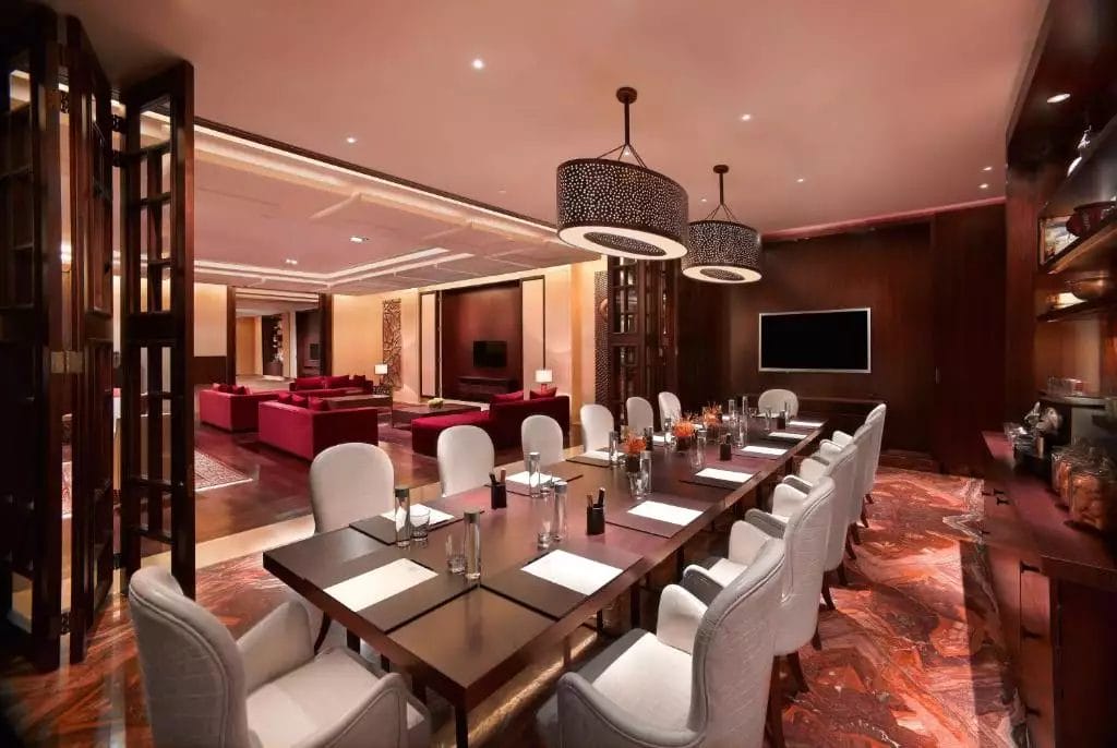 Sala da pranzo elegante e moderna nel Grand Hyatt Dubai, con un lungo tavolo apparecchiato per il pasto, fiancheggiato da morbide sedie e illuminazione ambientale.