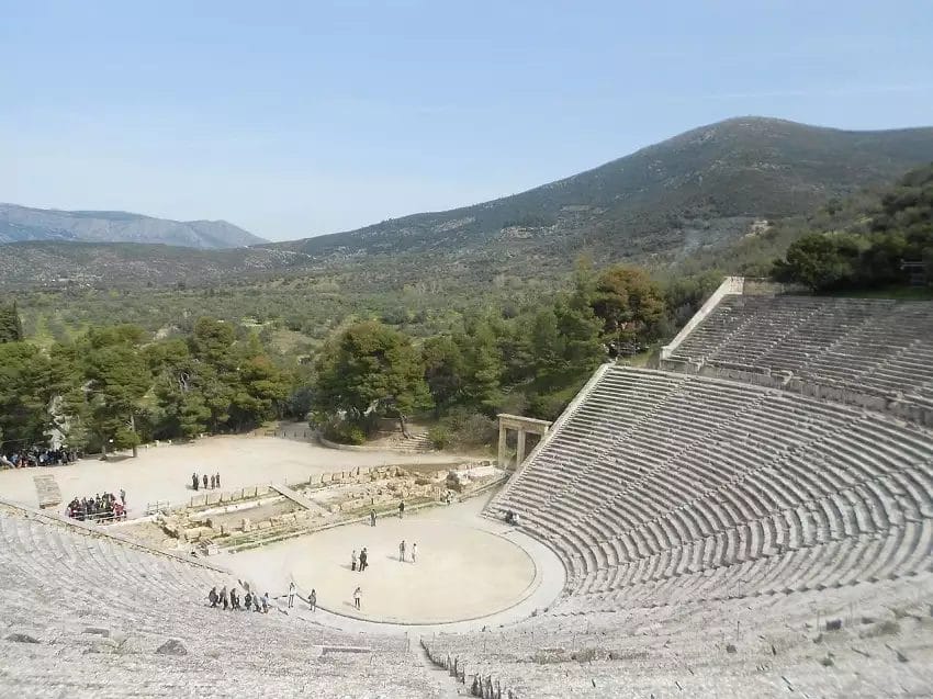 Antico anfiteatro immerso in un tranquillo paesaggio naturale con visitatori che ne esplorano la grandezza senza tempo nella Grecia Classica.