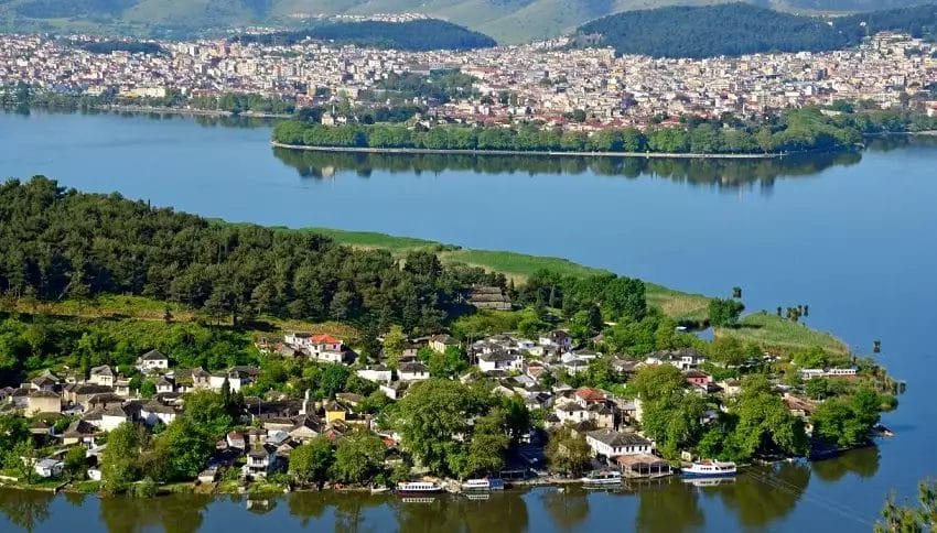 Una pittoresca veduta aerea di una penisola verde lussureggiante che si estende fino alle tranquille acque blu, con un pittoresco villaggio annidato lungo le sue rive e un vivace paesaggio urbano sullo sfondo, che incapsula l'essenza del "Tour G".