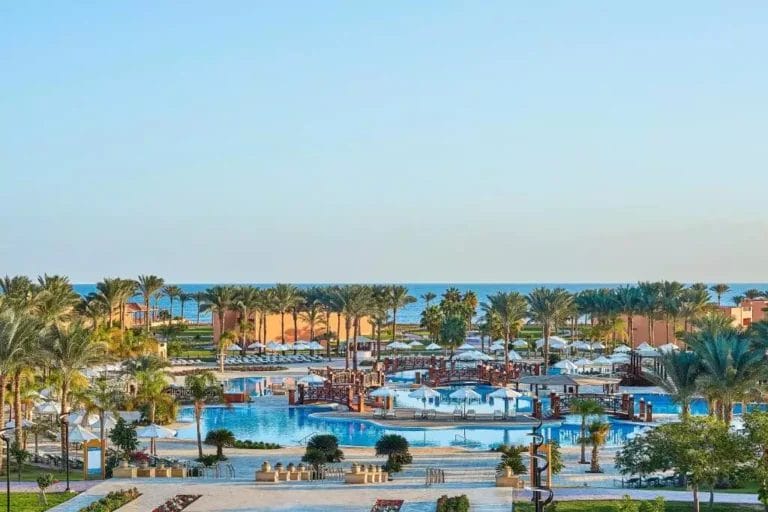 Una vista tranquilla sul resort JAZ GRAND MARSA che mostra un'oasi serena con piscina circondata da rigogliose palme con il mare calmo che si estende all'orizzonte durante una bella giornata limpida.