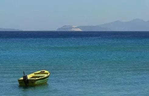 Una barca gialla solitaria che galleggia sulle calme acque blu con le lontane colline di Kipriotis Hippocrates all'orizzonte.