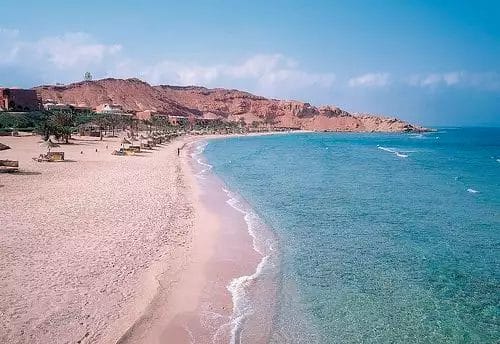 Una spiaggia tranquilla con acque limpide, spiaggia sabbiosa e scogliere rocciose sullo sfondo, conosciuta come Dream Lagoon Resort.