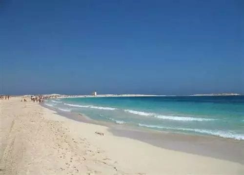 Almaza Beach Resort, una spiaggia sabbiosa con acque cristalline sotto un cielo luminoso.