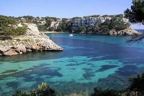 Una baia tranquilla con limpide acque aguamarina circondata da scogliere rocciose e vegetazione verde.